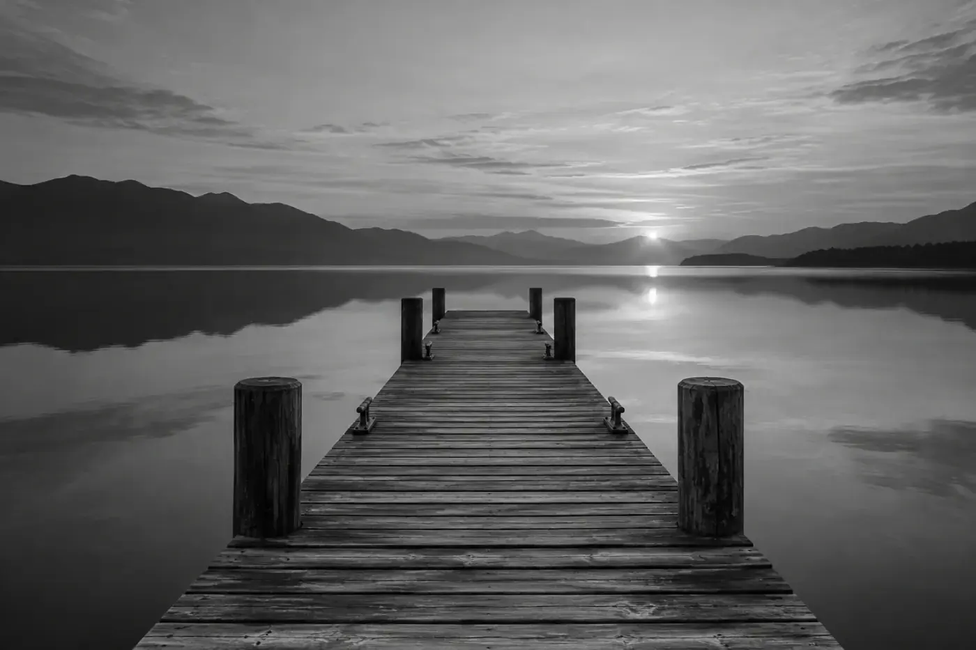 Fotografía en blanco y negro de un muelle de madera que se adentra en aguas tranquilas al amanecer